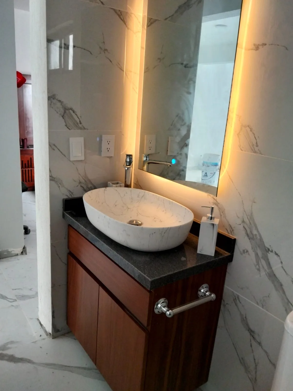 Lavabo de cubierta oscura con mueble de madera y espejo iluminado